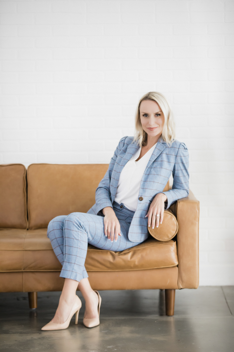 Woman in blue suit and tan high heels sitting on tan couch.